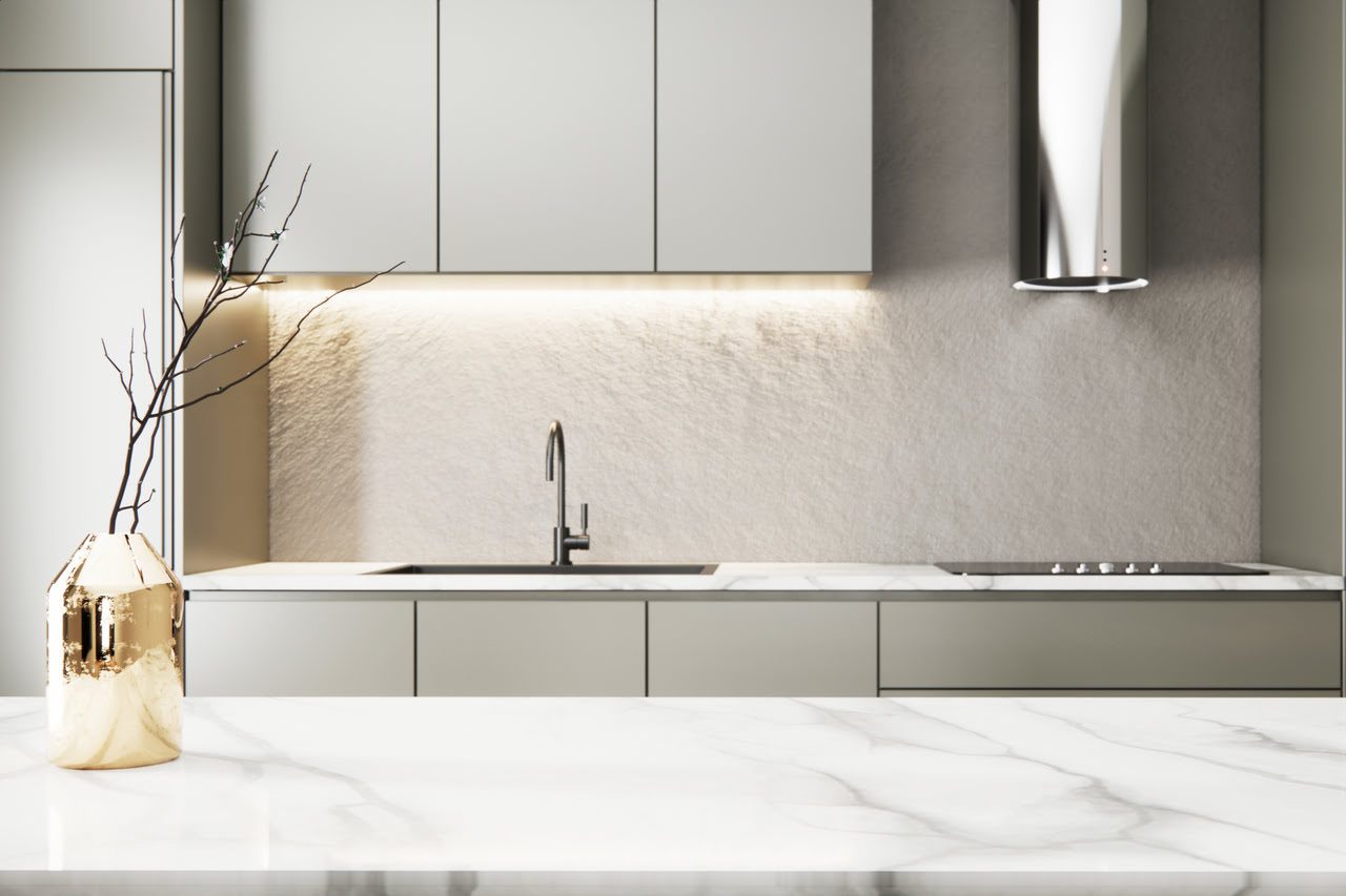 Modern kitchen with light gray cabinets, marble countertop, metal range hood, and under-cabinet lighting. A gold vase with twigs sits on the counter.