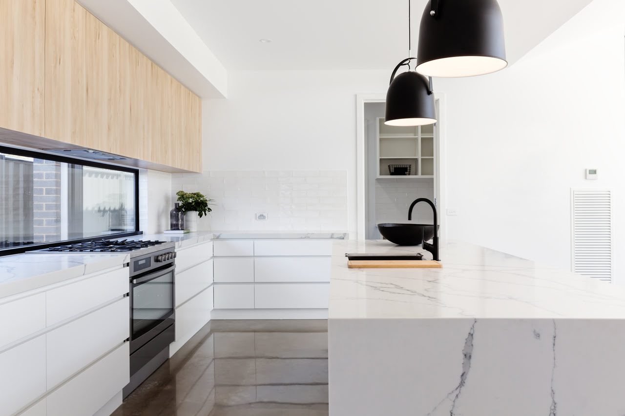 Modern kitchen with white cabinetry, marble countertops, stainless steel appliances, a black sink, and pendant lighting.