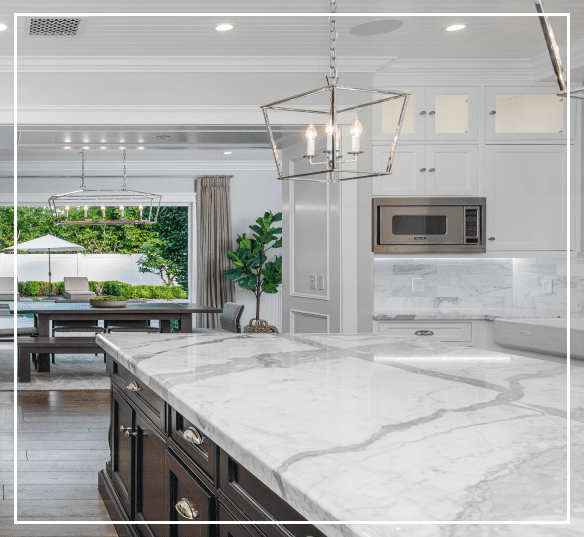 Modern kitchen with a marble island, white cabinetry, and stainless steel appliances. A dining area with glass doors is visible in the background.