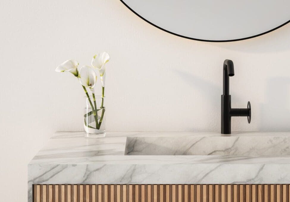 Modern bathroom sink with a marble countertop and black faucet. A small vase with white calla lilies is next to the sink.